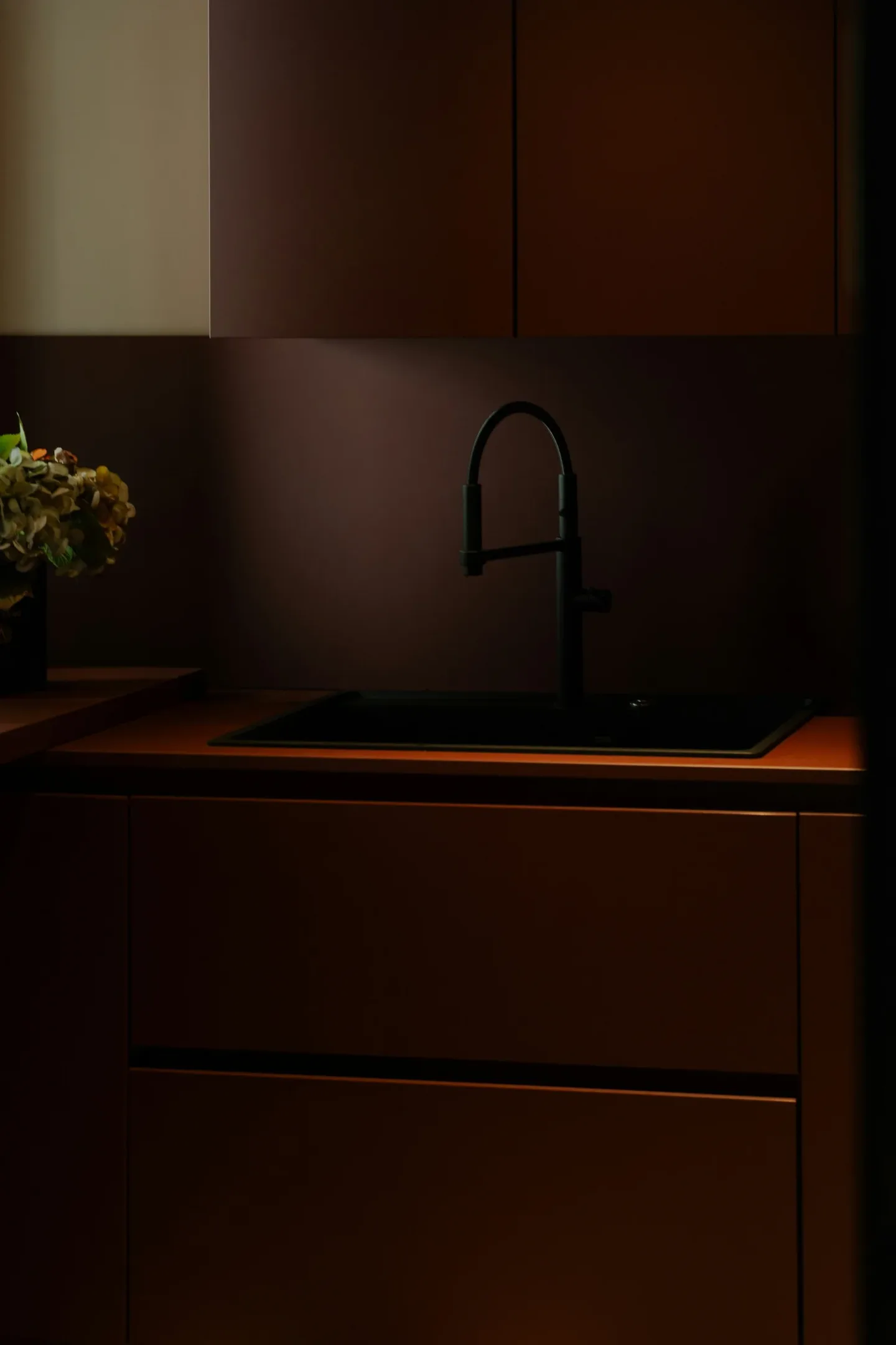 A kitchen with dark wood cabinets, a black faucet over a sink, and a flower arrangement on the left side.
